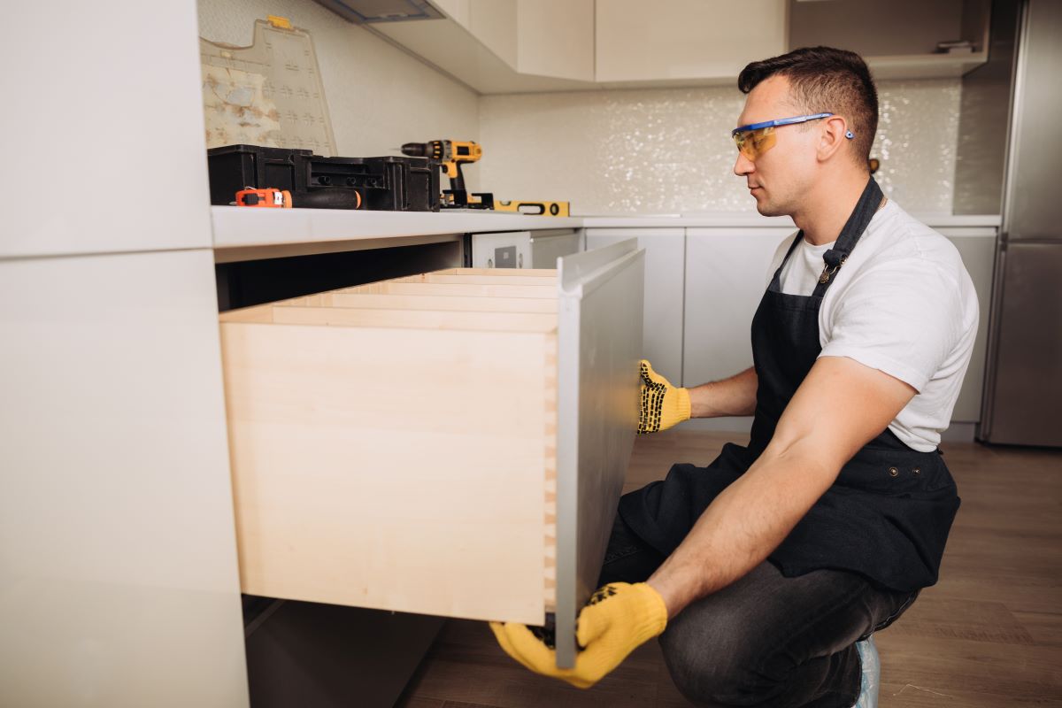 Hire Professional Cabinet Installer Services | Dr. Cabinet 4 Worker wearing gloves and safety glasses is installing a large drawer in a modern kitchen cabinet.